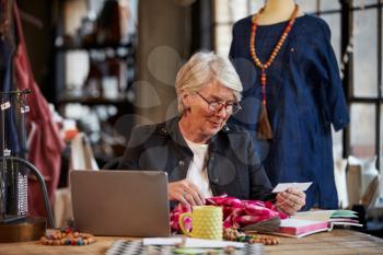 Female Fashion Designer Working At Laptop In Studio