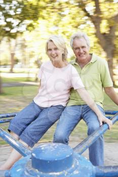 Senior Couple Riding On Roundabout In Park