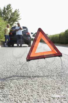 Couple Broken Down On Country Road With Hazard Warning Sign In Foreground