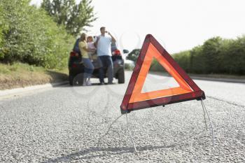 Family Broken Down On Country Road With Hazard Warning Sign In Foreground