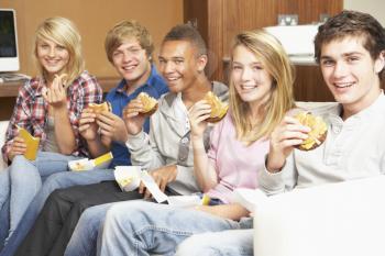 Group Of Teenage Friends Sitting On Sofa At Home Eating Fast Food