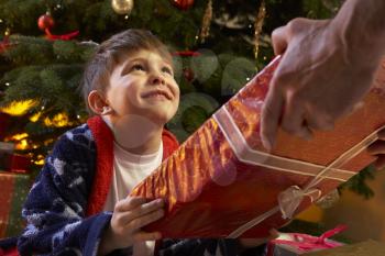 Young Boy Receiving Christmas Present In Front Of Tree