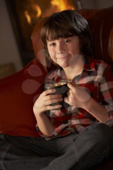 Young Boy Relaxing With Hot Drink By Cosy Log Fire