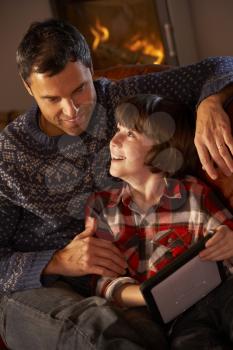 Father And Son Using Tablet Computer By Cosy Log Fire