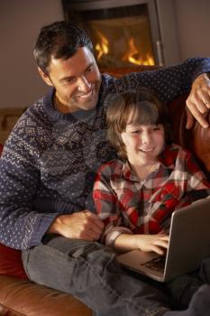 Father And Son Using Laptop Computer By Cosy Log Fire