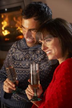 Middle Aged Couple Sitting Sofa By Cosy Log Fire With Glass Of Champagne