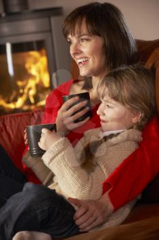 Mother And Daughter Relaxing With Hot Drink Watching TV By Cosy Log Fire