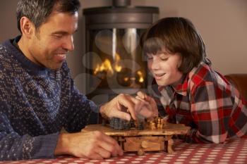 Father And Son Playing Chess By Cosy Log Fire