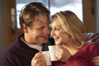 Middle Aged Couple Sitting On Sofa With Hot Drinks