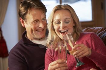 Middle Aged Couple Sitting On Sofa With Glasses Of Champagne