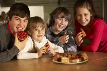 Group Of Children Enjoying Plate Of Cakes In Kitchen