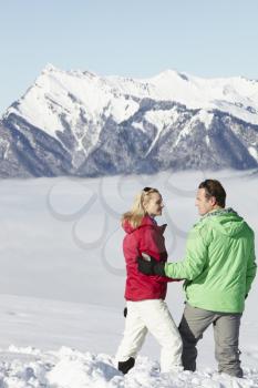 Couple Admiring Mountain View Whilst On Ski Holiday In Mountains