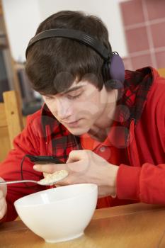 Teenage Boy Listening To MP3 Player Whilst Eating Breakfast