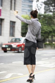 Businesswoman Hailing Taxi In Busy Street