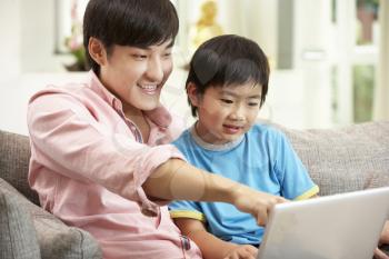 Chinese Father And Son Using Laptop Whilst Relaxing On Sofa At Home