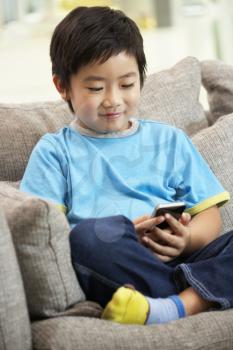 Young Chinese Boy Using Mobile Phone On Sofa At Home