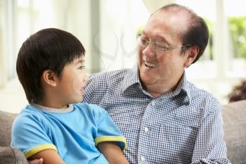 Chinese Grandfather And Grandson Relaxing On Sofa At Home