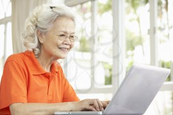 Senior Chinese Woman Sitting At Desk Using Laptop At Home