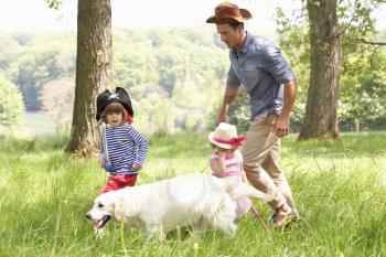 Father Playing Exciting Adventure Game With Children And Dog In Summer Field