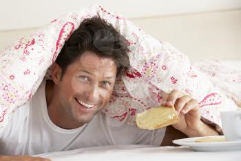 Man Snuggled Under Duvet Eating Breakfast