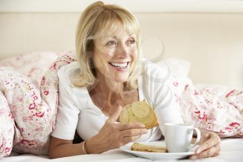 Senior Woman Snuggled Under Duvet Eating Breakfast