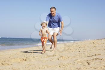 Grandfather And Grandson Running Along Beach