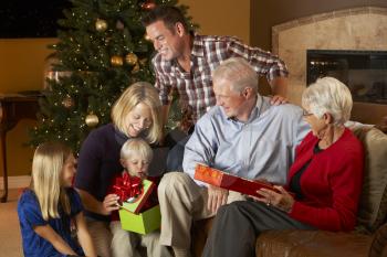 Multi Generation Family Opening Christmas Presents In Front Of Tree