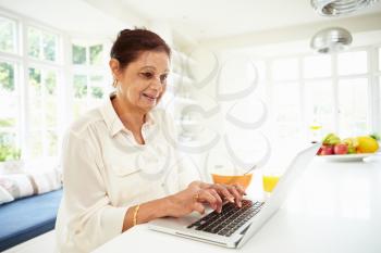 Senior Indian Woman Using Laptop Whilst Eating Breakfast