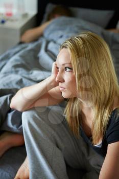 Sad Teenage Girl Sitting In Bedroom Whilst Boyfriend Sleeps