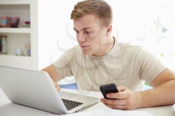 Teenage Boy Sending Text Message Whilst Studying On Laptop