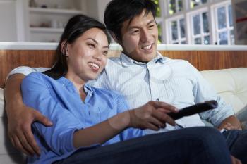 Asian Couple Sitting On Sofa Watching TV Together