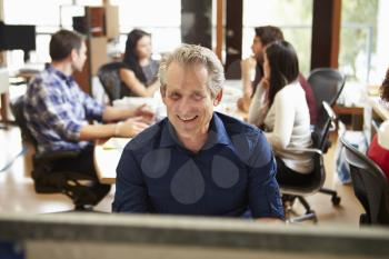 Businessman Working At Desk With Meeting In Background