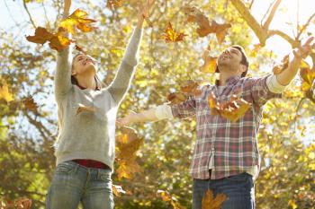 Couple Throwing Autumn Leaves In The Air
