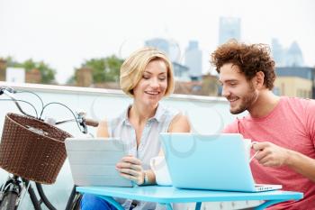 Couple On Roof Terrace Using Laptop And Digital Tablet