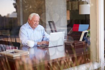 View Of Senior Man Using Laptop Through Window