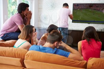 Group Of Friends Sitting On Sofa Watching Soccer Together