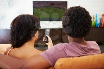 Rear View Of Couple Sitting On Sofa Watching TV Together