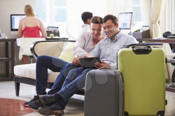 Male Couple Sitting In Hotel Lobby Looking At Digital Tablet