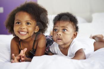 Sister With Baby Brother Lying On Parent's Bed