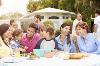 Multi Generation Family Enjoying Meal In Garden Together