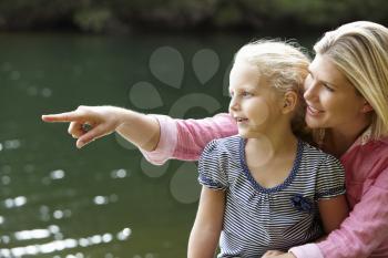 Mother and young daughter sitting by lake