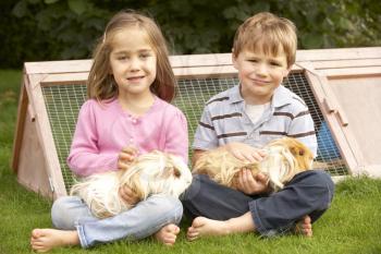 Young boy and girl in garden holding guinea pigs