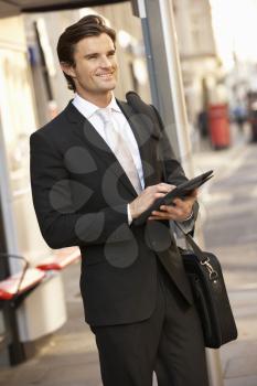 Businessman standing at bus stop using tablet