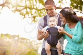 Family With Baby Son In Carrier Walking Through Park