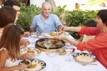 Multi Generation Family Enjoying Meal On Terrace Together