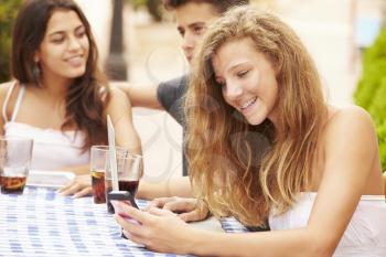 Teenage Girl Using Mobile Phone Sitting At Caf With Friends