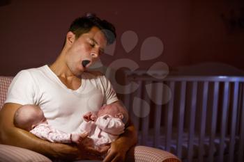 Tired Father At Home Cuddling Twin Baby Daughters In Nursery