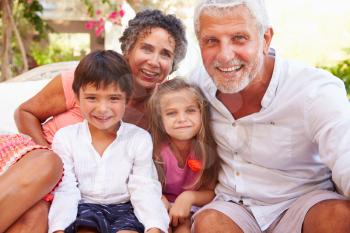 Grandparents With Grandchildren Sitting On Seat In Garden