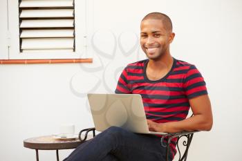 Young Man Sitting Outdoors With Laptop And Drinking Coffee