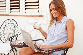 Young Woman Sitting Outdoors With Laptop And Drinking Coffee